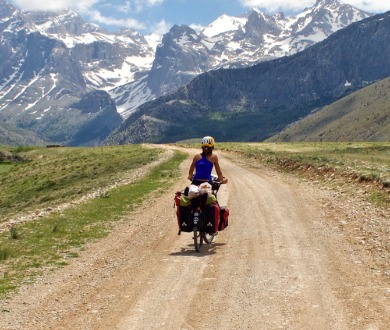 Photographie: Une femme, de dos, sur un vélo de voyage, quelque part dans un paysage montagneux. 